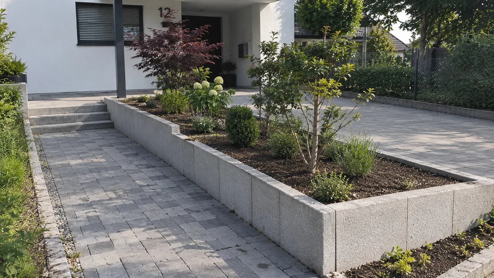 Moderner Vorgarten mit Granit-Hochbeet, Pflasterweg und frischer Bepflanzung – Garten- und Landschaftsbau